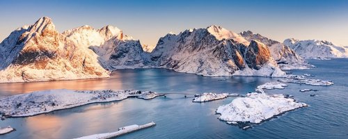 Amazing aerial view of Lofoten Islands nature from drone, winter sunrise snowy scenery of village Reine, Sakrisoy and Hamnoy during beautiful mountain ridge with alpenglow, scene over polar circle.